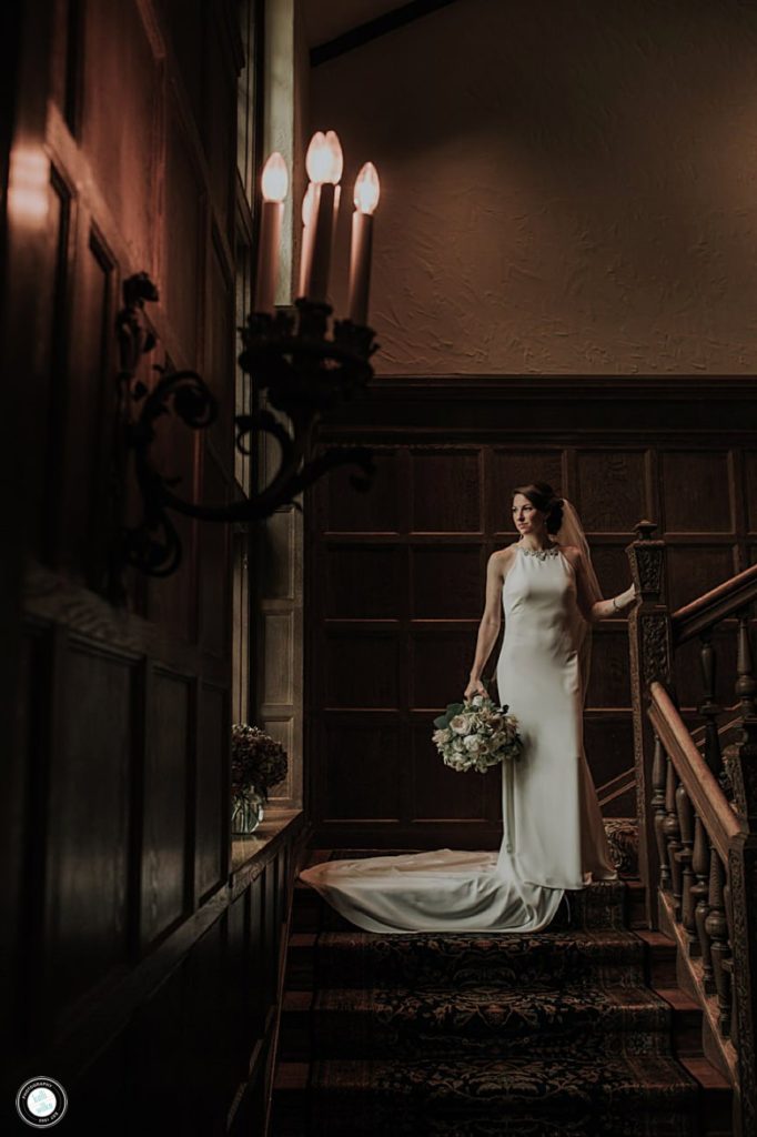 bride portrait looking out the window while standing on the stairs in her fitted wedding gown just before her wedding at greenville country club in wilmington de