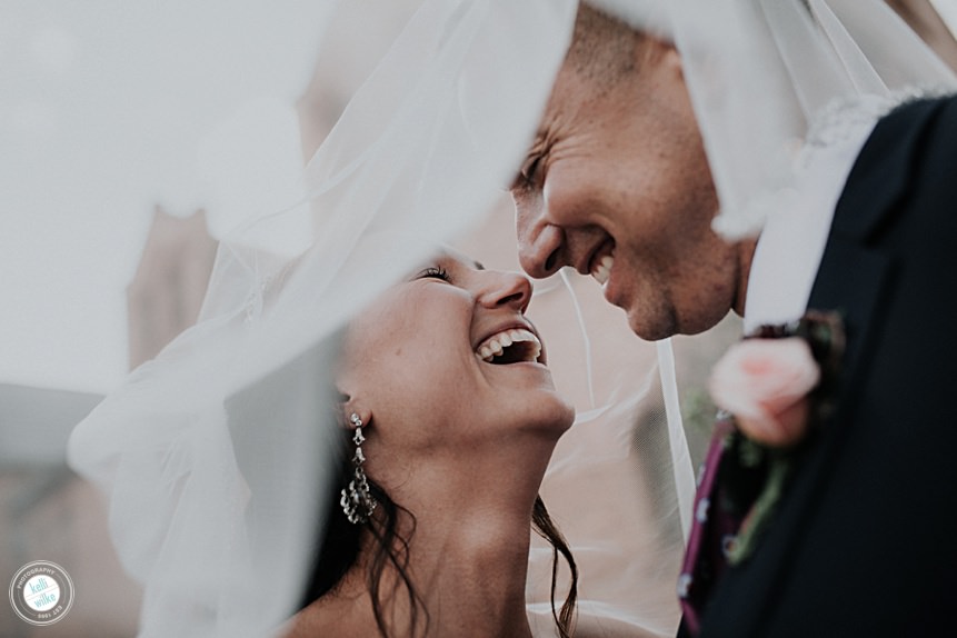 couple poses under the brides veil on their wedding day