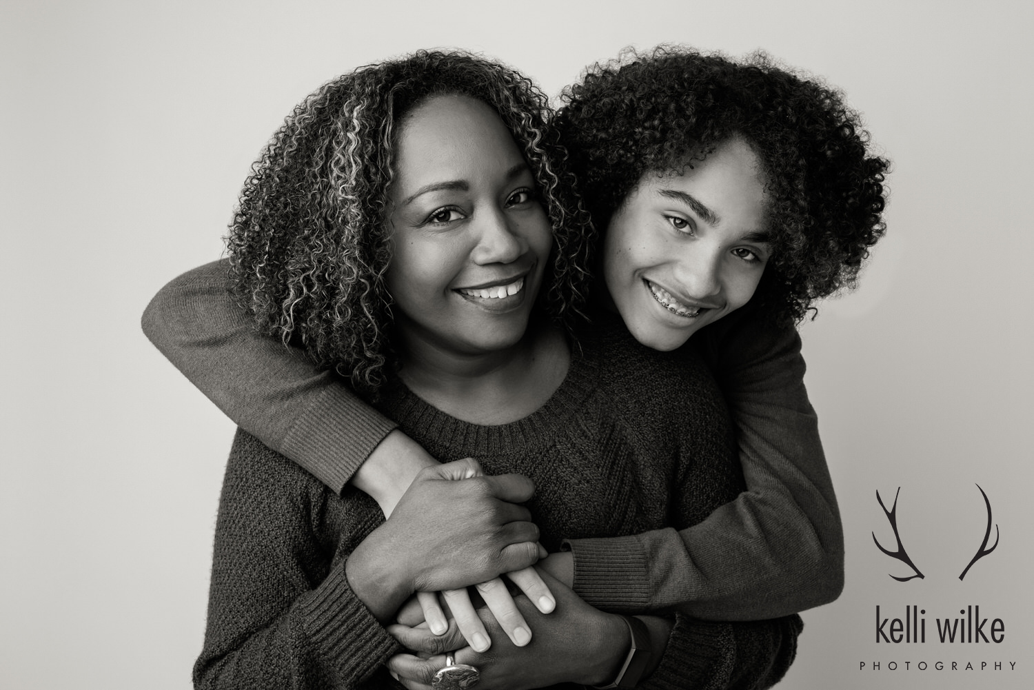 A black and white picture of a child hugging their mom, both smiling at the camera. 