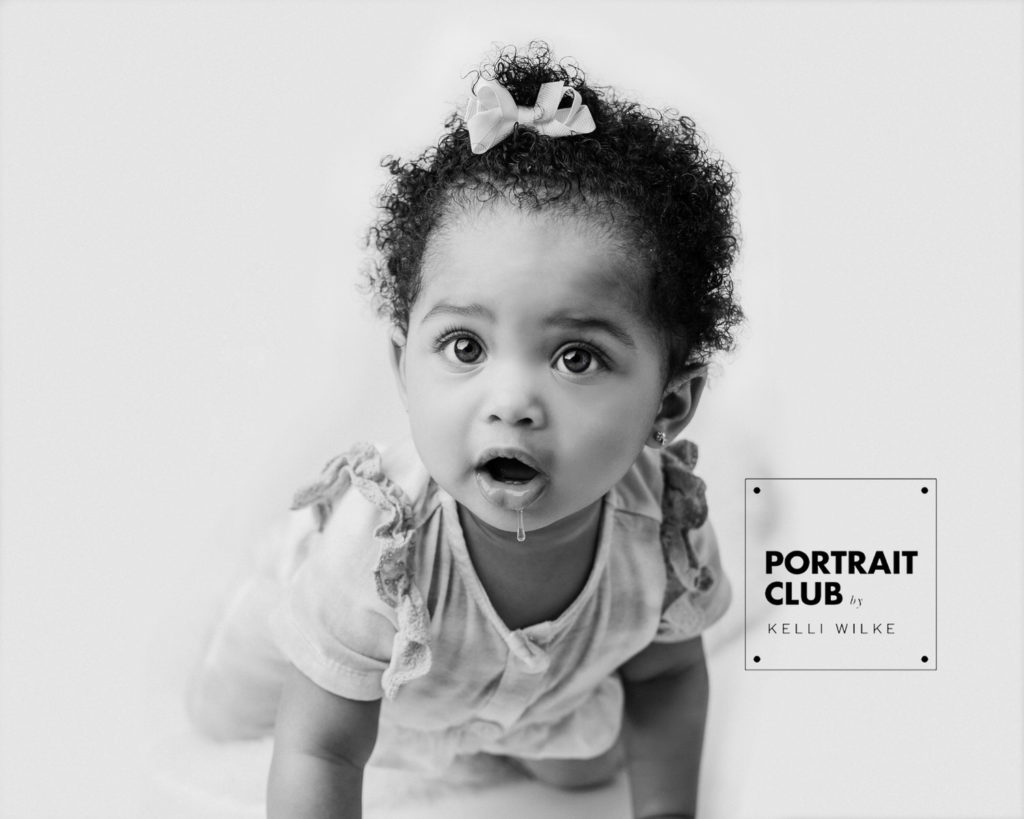 A candid picture of a little girl crawling towards the camera, her eyes wide open and drool dropping off her chin during a studio portrait session with Portrait Club by Kelli Wilke in Wilmington, DE. 